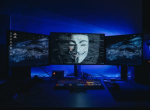 Computer screens with a dark ominous mask figure. 